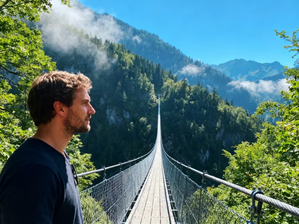 Mężczyzna podziwiający widok z wiszącego mostu Sky Bridge 721 rozciągającego się nad zieloną górską doliną.