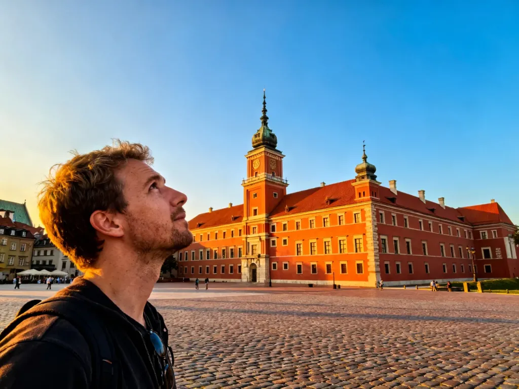 Zamek Królewski w Warszawie o zachodzie słońca z turystą podziwiającym zabytkową fasadę budynku.