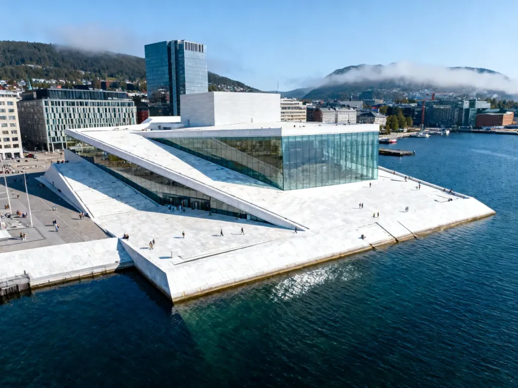 Opera w Oslo z charakterystycznym białym dachem schodzącym do wód fiordu na tle nowoczesnej zabudowy miasta.