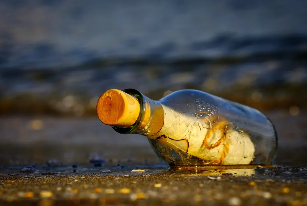 Wiadomość w butelce leżąca na piaszczystej plaży w Międzyzdrojach na tle morza.