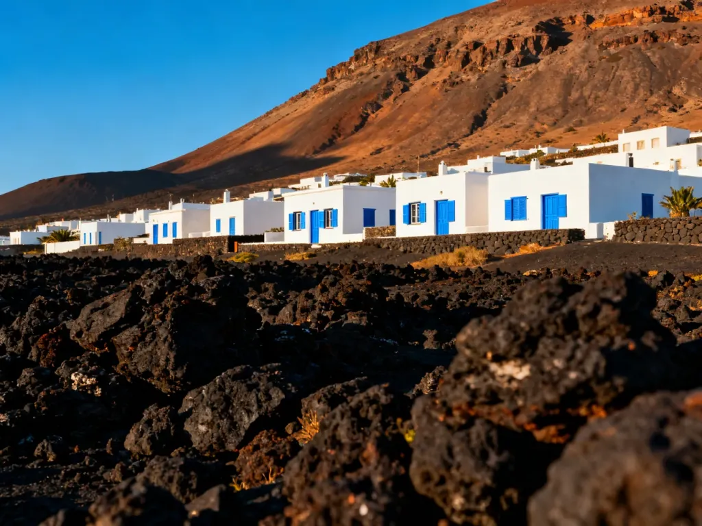 Panoramiczny widok na wulkaniczny krajobraz Lanzarote z tradycyjną białą zabudową na tle surowych gór.